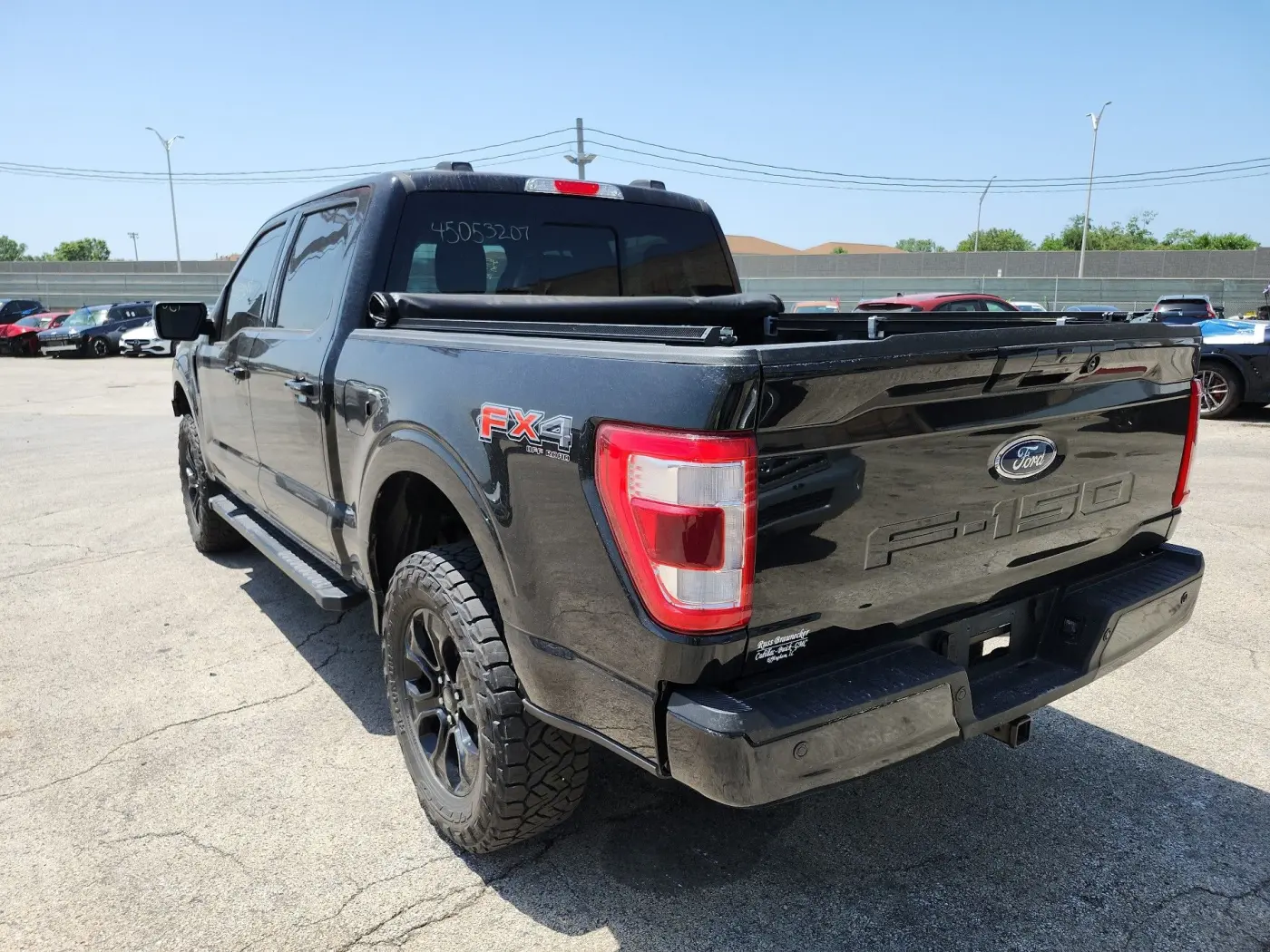 Czarny Ford F-150 FX4 widziany z tyłu z lewej strony, z roletą na skrzyni ładunkowej, na asfaltowym placu aukcyjnym