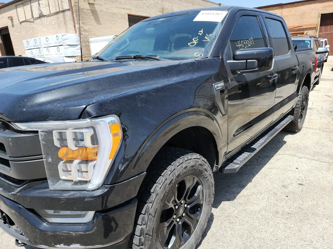 Czarny Ford F-150 Lariat widziany z przodu z lewej strony, na placu aukcyjnym, z nalepką z numerem lotu na szybie