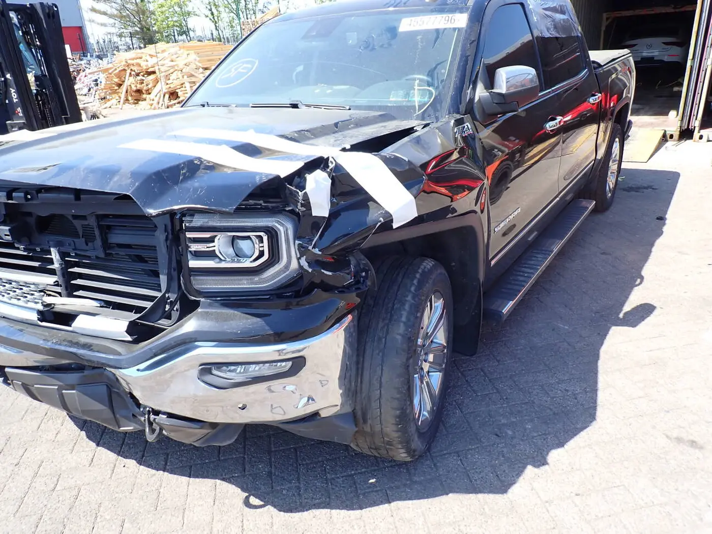 Czarny GMC Sierra Z71 z uszkodzonym przodem: pogięta maska, wyrwany reflektor i zerwany zderzak z taśmą ochronną