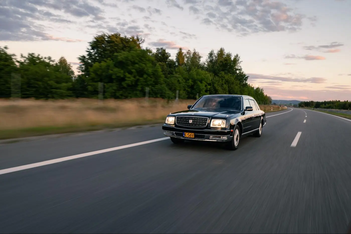 Czarna Toyota Century w jeździe po drodze o zachodzie słońca, widok z przodu